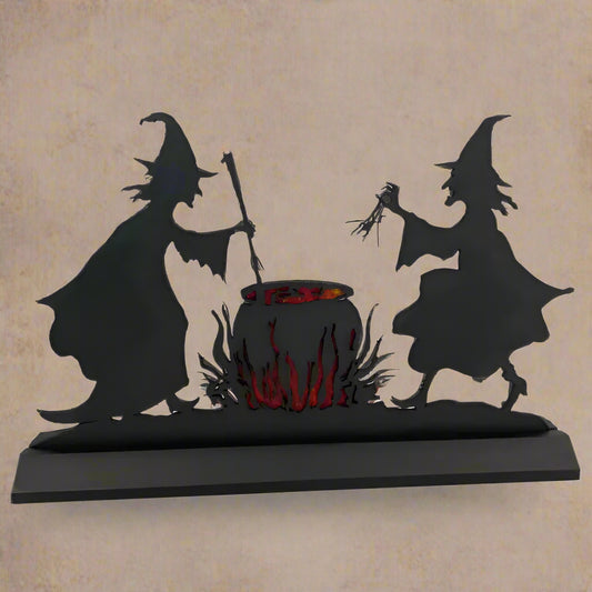 A silhouette of two witches with a cauldron in the center, with orange fire and witch's brew around it, set against a black background.