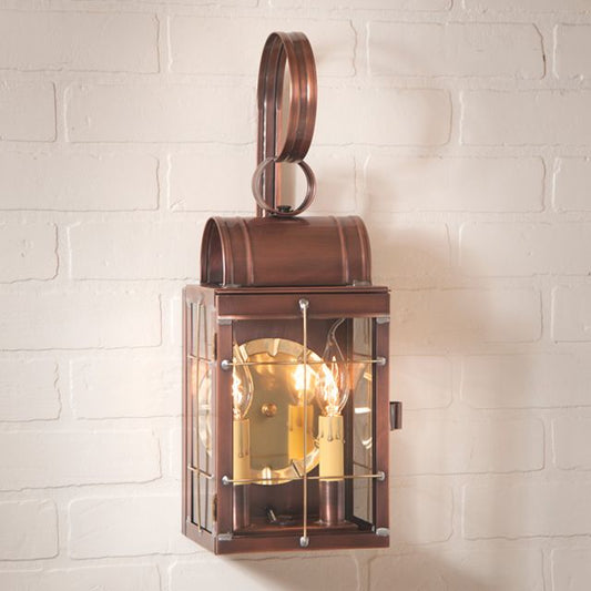 Antique copper double wall lantern with clear glass and brass hardware, mounted on a white brick wall.
