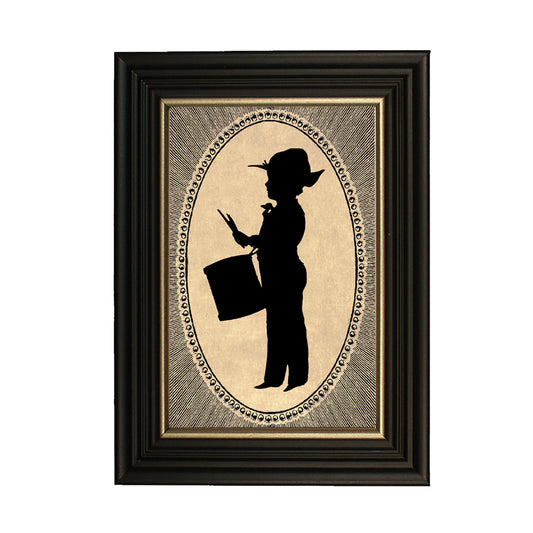 A framed silhouette illustration of a drummer boy in a black wood frame with gold trim, set against a craft paper backdrop.