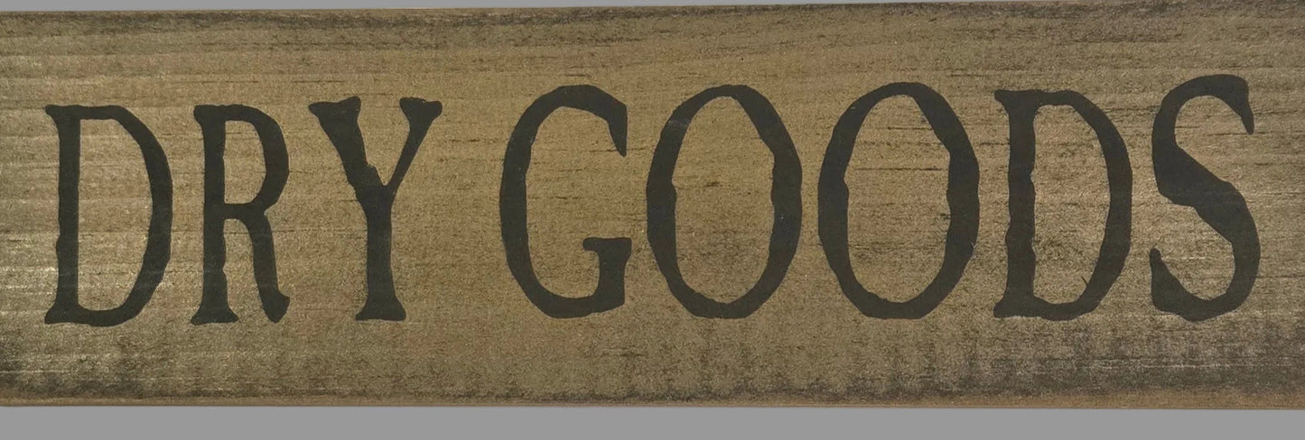 Wooden sign with 'DRY GOODS' text on a gray background