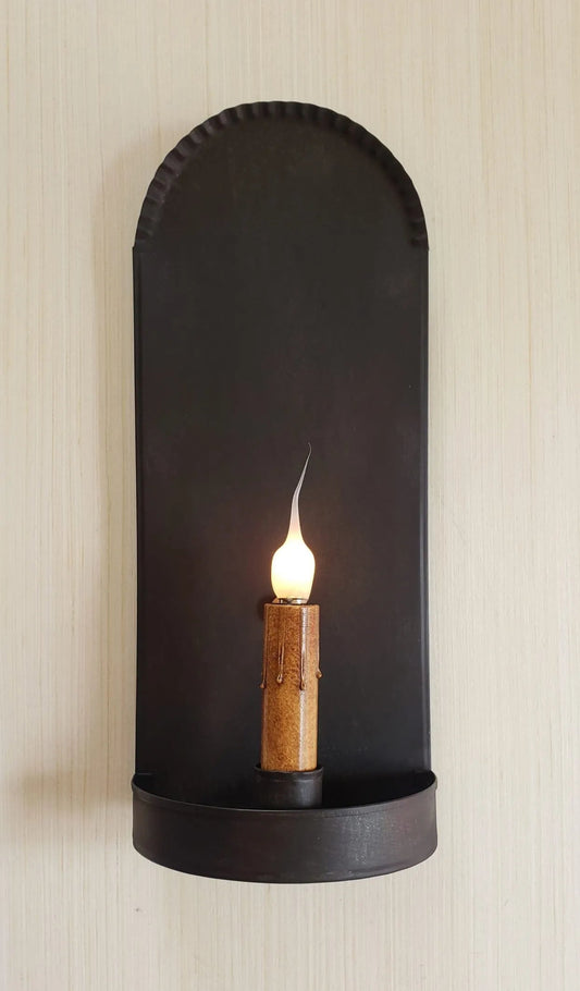 Black wall-mounted candle holder with a lit candle on a beige wall.
