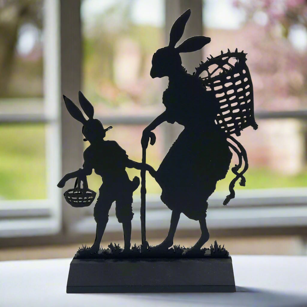 A flat black silhouette of two Easter bunnies, one carrying a basket, placed on a solid wood base.