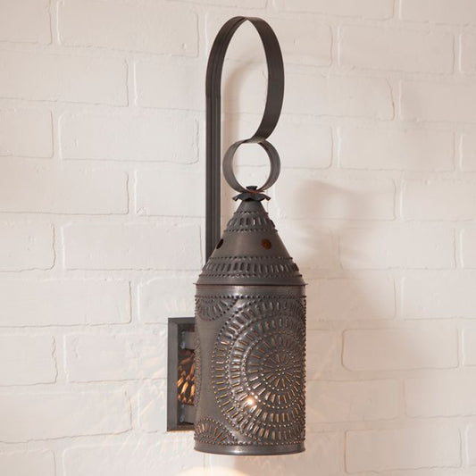 A black electrified wall lantern with a kettle-shaped design, mounted on a white brick wall.
