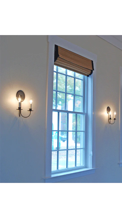 Two lit sconces flanking a window with a pull  down shade.