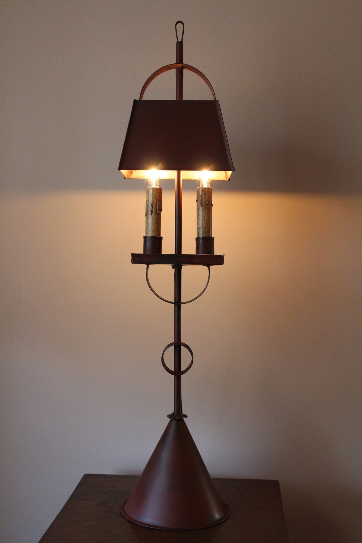 Shaded tin table lamp on a square table in front of a cream colored wall.