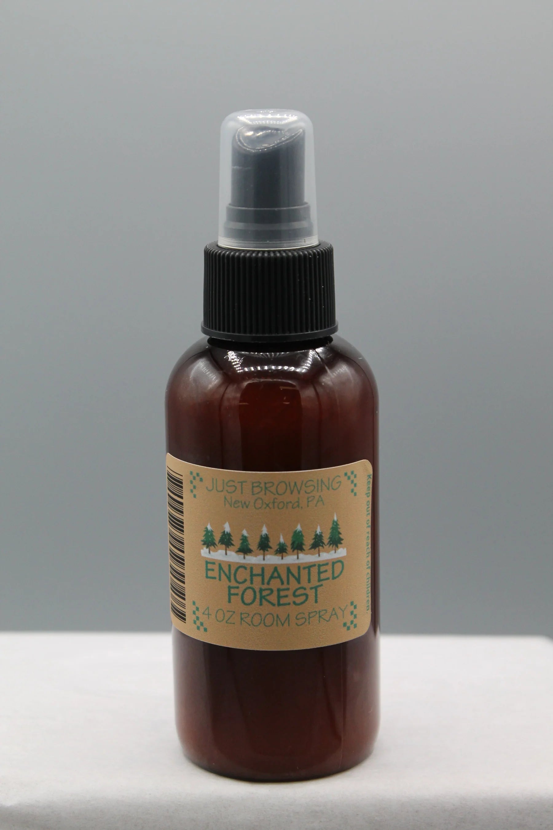 A 4oz bottle of Enchanted Forest room spray with a mist spray top. The bottle is brown with a label that has green text and a Christmas tree graphic, indicating a holiday-themed fragrance.