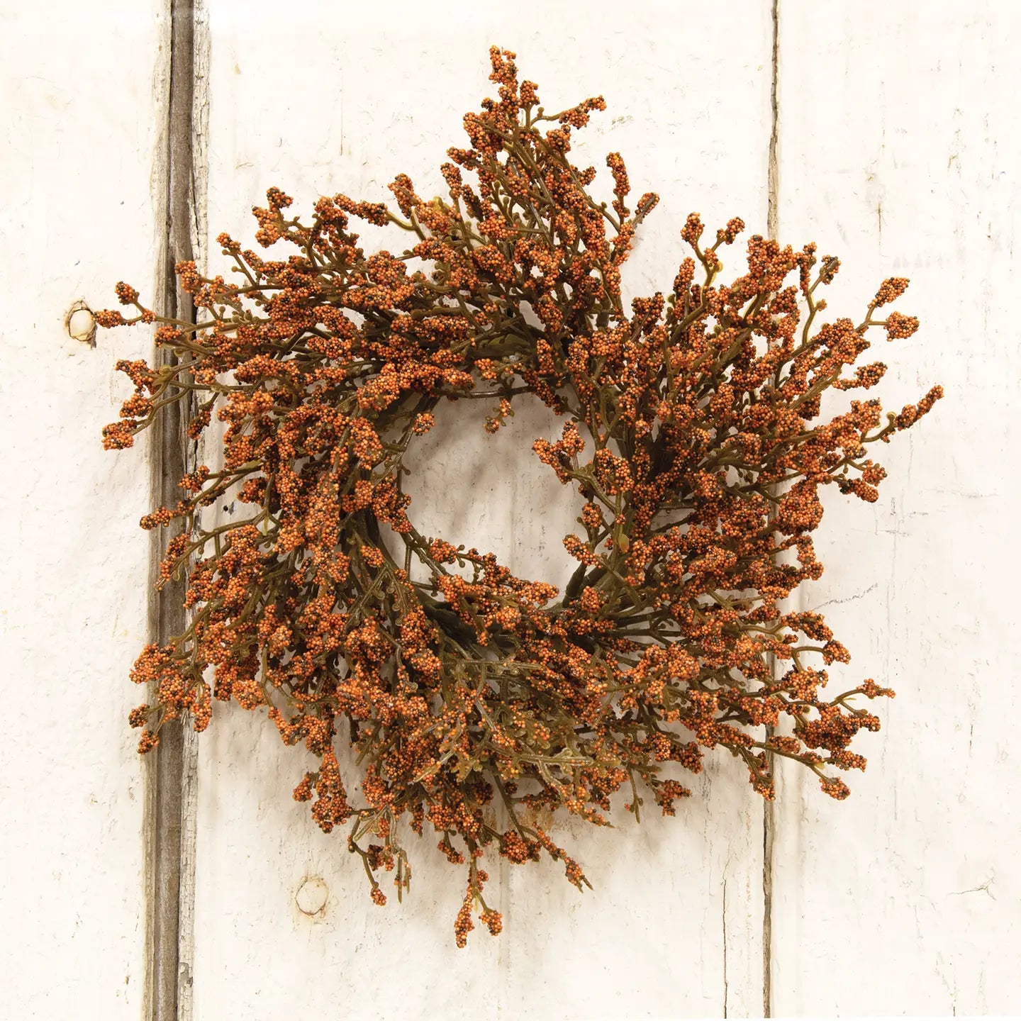 Decorative wreath with orange berries on a white wooden door