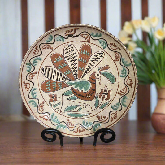 Decorative redware plate with a bird design on a stand, with flowers in the background.