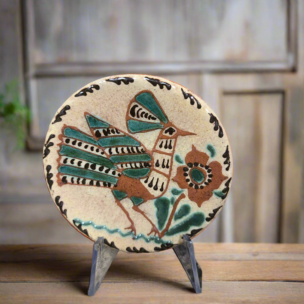 Small round redware plate with a fancy feathered bird and flower with warm green, yellow and brown hues