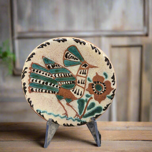 Small round redware plate with a fancy feathered bird and flower with warm green, yellow and brown hues