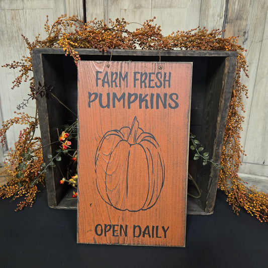 Wooden sign with 'Farm Fresh Pumpkins' text and pumpkin illustration on a rustic wooden surface.