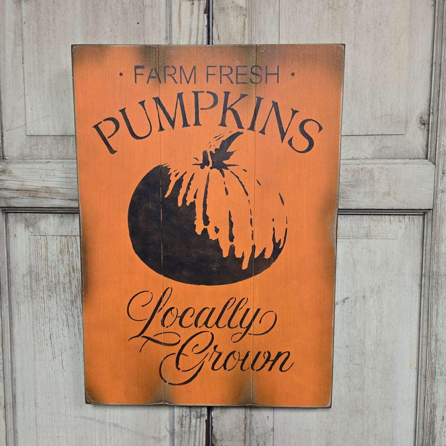 A wooden sign with an orange background, featuring the text 'Farm Fresh Pumpkins' and a pumpkin graphic, placed against a door.