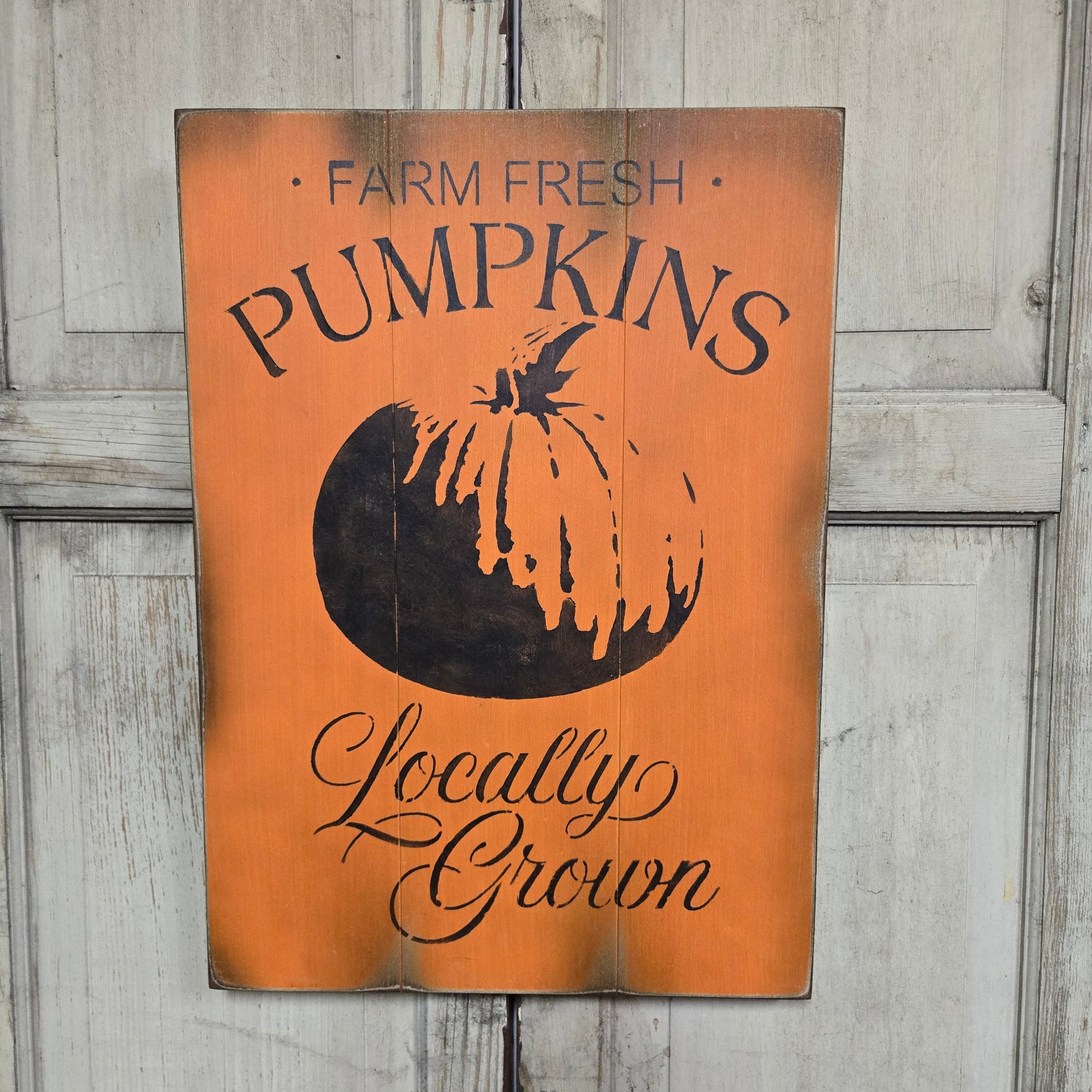 A wooden sign with an orange background, featuring the text 'Farm Fresh Pumpkins' and a pumpkin graphic, placed against a door.