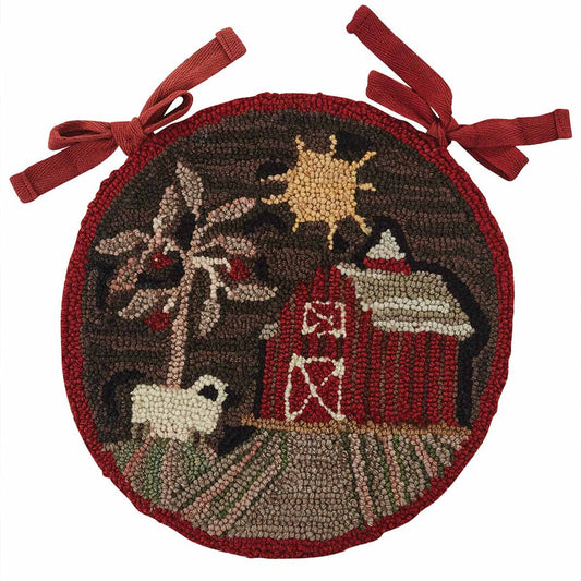 A round, hooked chair pad with a barn and sheep design, featuring a brown base with a red border and sun motif in the center.