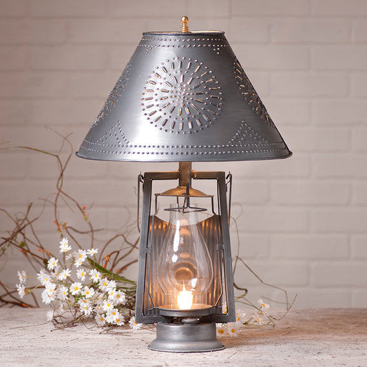 Decorative lantern with a patterned shade on a wooden surface with flowers in the background