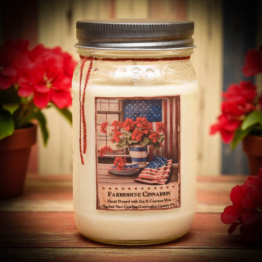 A 16 oz Mason jar candle with a label featuring a patriotic theme, including the American flag and flowers, set on a table with red flowers in the background.