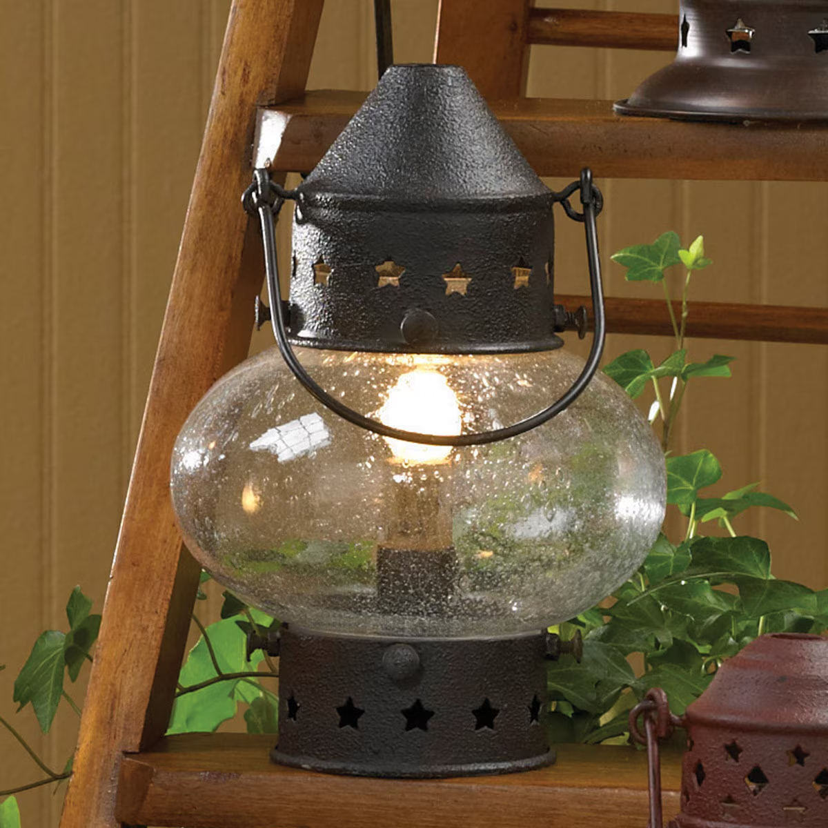 A Fat Onion Lamp with a metal base and an onion-shaped glass shade, providing a warm glow. The lamp is placed on a wooden step ladder with a plant beside it.