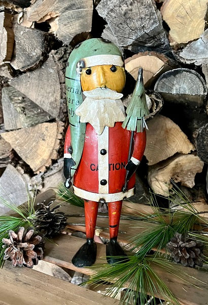 A metal statue of Father Christmas holding a toy rocket, with a red jacket, white beard, and green hat, standing on a pine cone decoration.