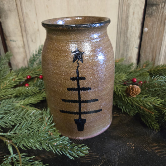 Brown ceramic vase with black symbols on a wooden surface with greenery