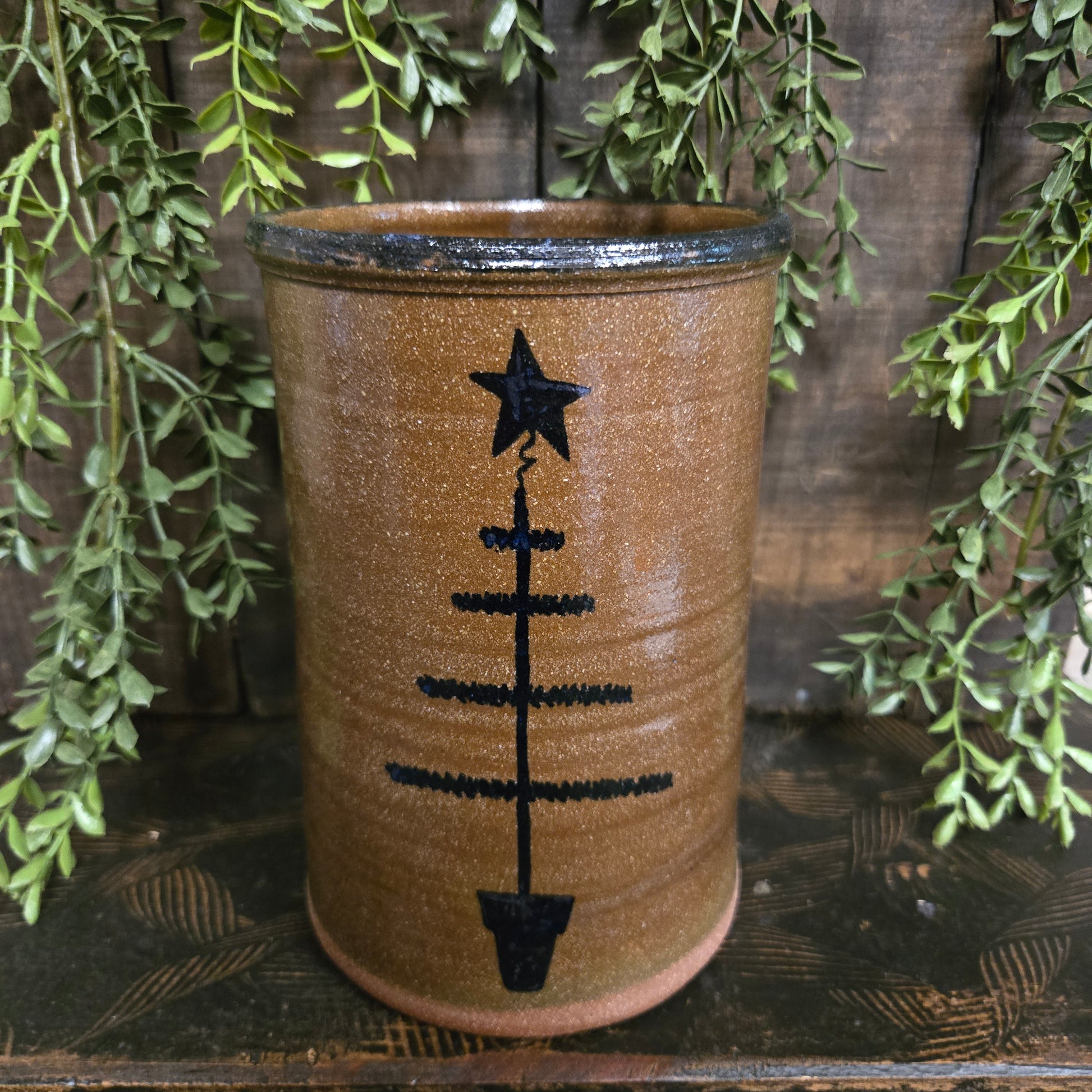 Stoneware crock with feather tree design on a wooden surface with green leaves.