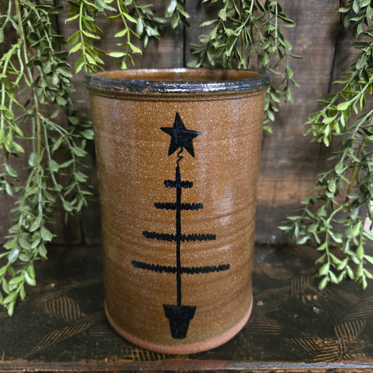 Stoneware crock with feather tree design on a wooden surface with green leaves.
