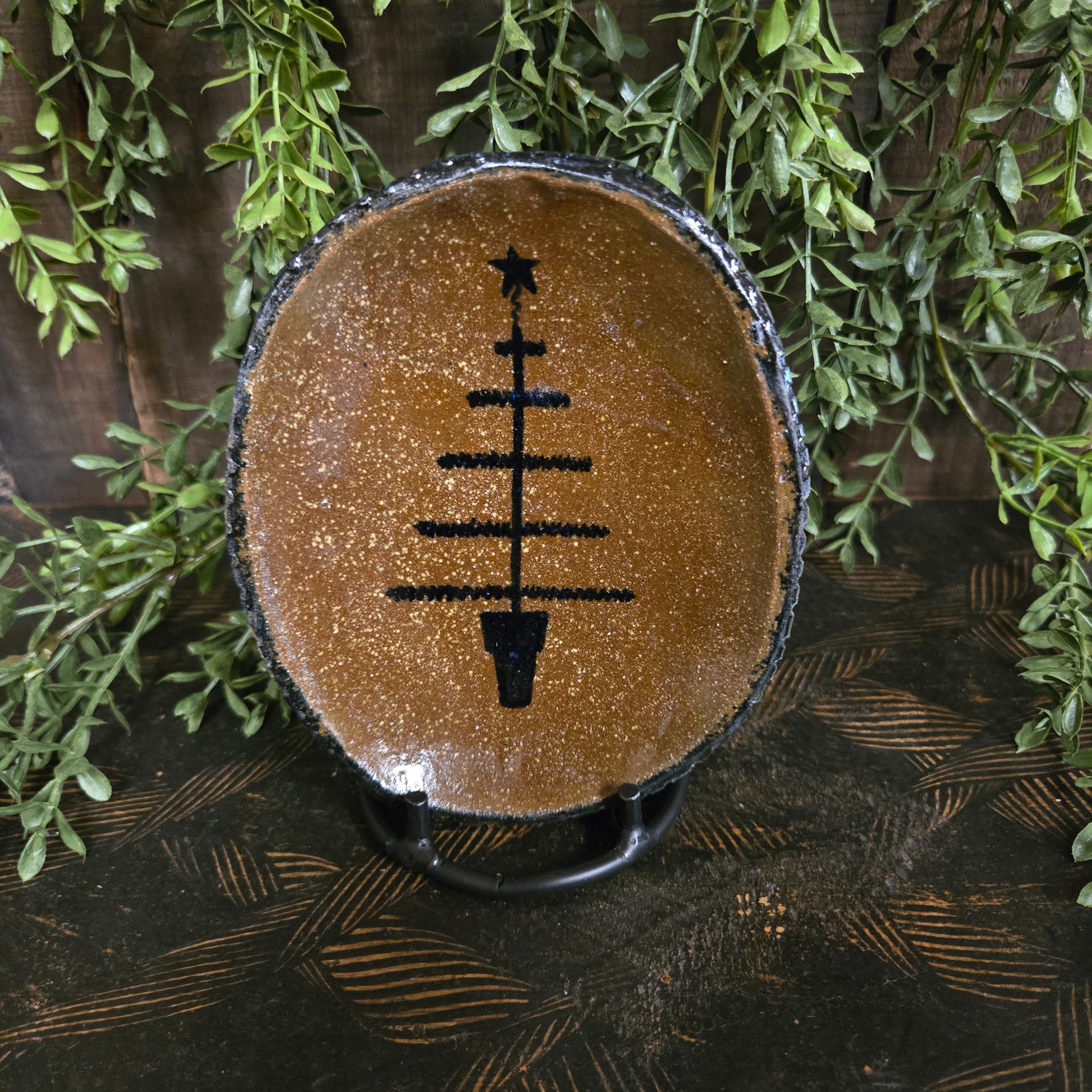 Small oval stoneware plate with feather tree and star motif on a textured wood surface