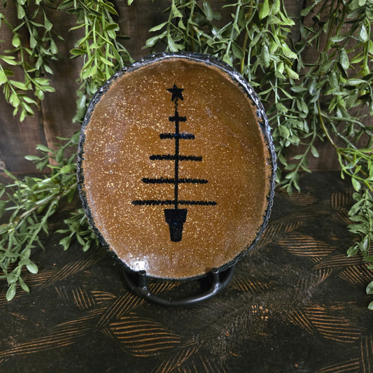 Small oval stoneware plate with feather tree and star motif on a textured wood surface