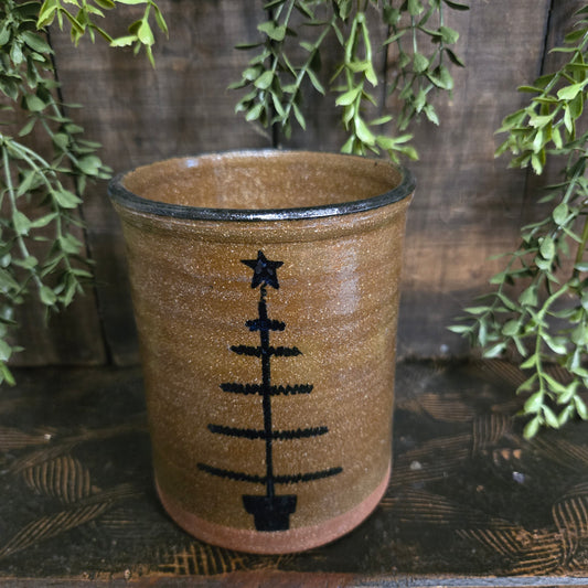 Decorative crock with feather tree motif on a wooden surface with greenery
