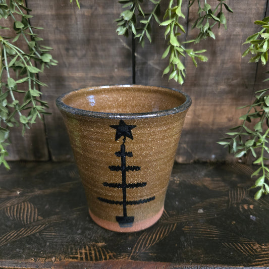 Decorative brown crock with feather tree motif on a wooden surface with greenery