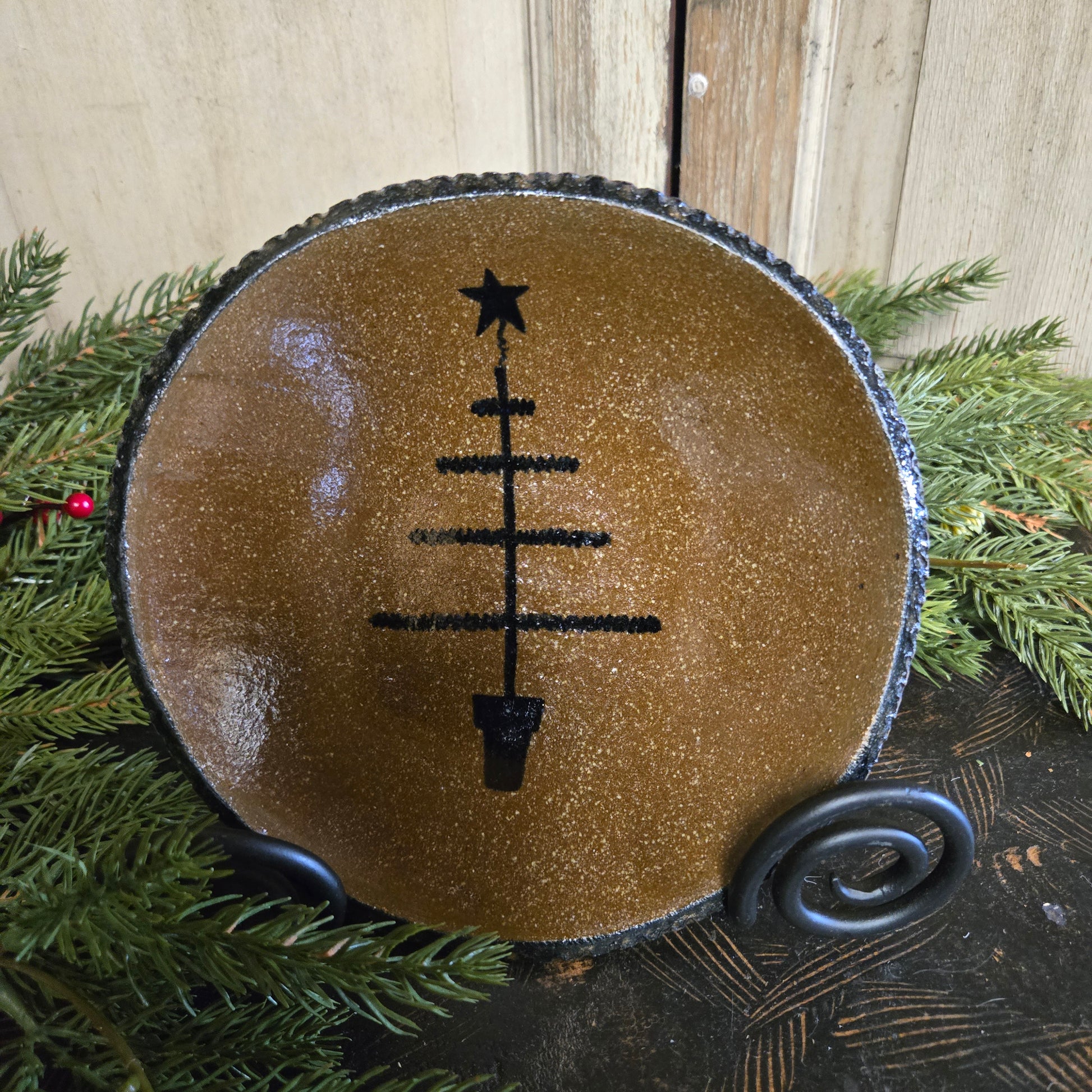 Decorative item with a black feather tree design on a brown background, surrounded by greenery.