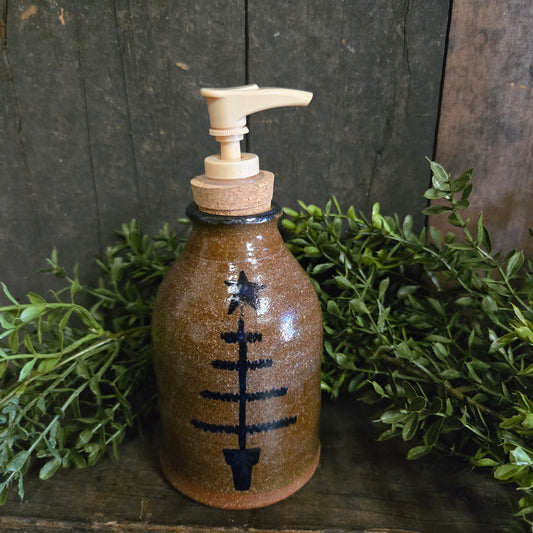 Ceramic bottle with pump and black feather tree design on a wooden surface with greenery