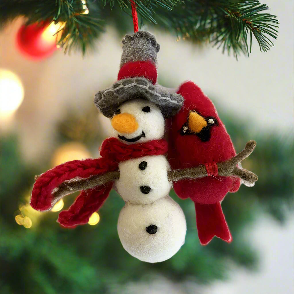 A felted wool ornament featuring a snowman and a cardinal bird, with the snowman wearing a gray hat and a red scarf, and the bird in a red outfit with a branch for a perch.