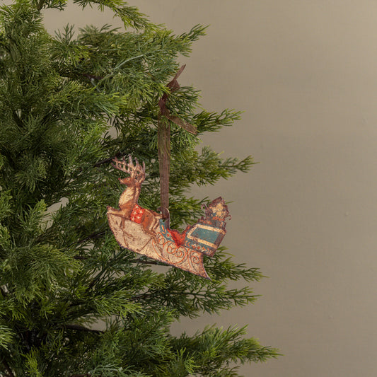Decorative reindeer ornament hanging on a Christmas tree branch against a plain background
