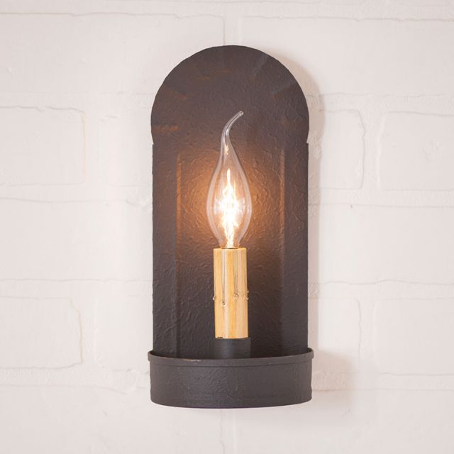 Black wall sconce with a lit bulb on a white brick wall background