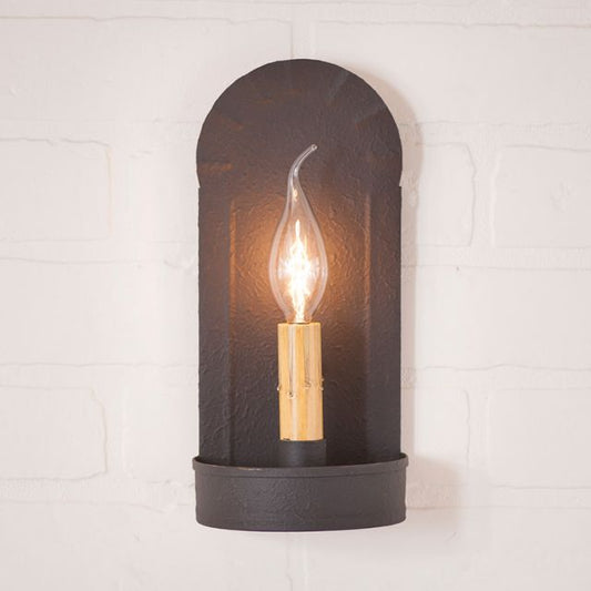 Black wall sconce with a lit bulb on a white brick wall background