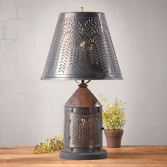 A kettle black finish fireside lamp with a willow shade, featuring a willow tree pattern on the shade and a harp included, placed on a wooden surface with a potted plant beside it.