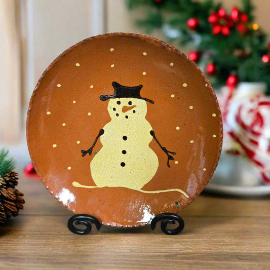 Decorative plate with a snowman design on a stand, Christmas tree in the background