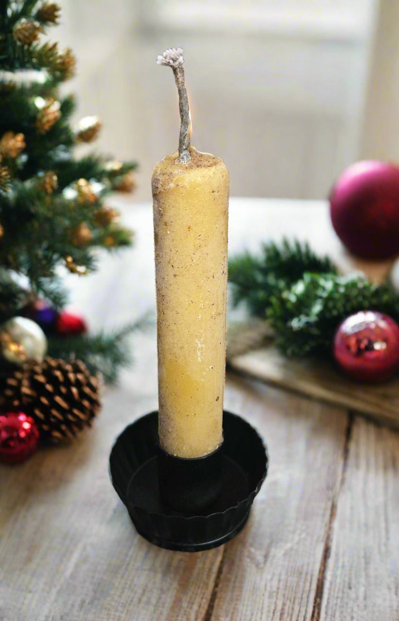 Candle in a holder on a wooden surface with Christmas decorations in the background