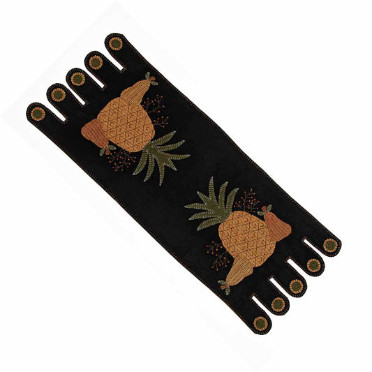 A black table runner with a folk art design featuring pineapples and tassels.