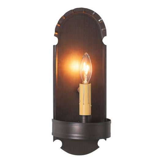 A wall-mounted foot sconce with a kettle black finish, featuring an incandescent bulb providing a warm glow.