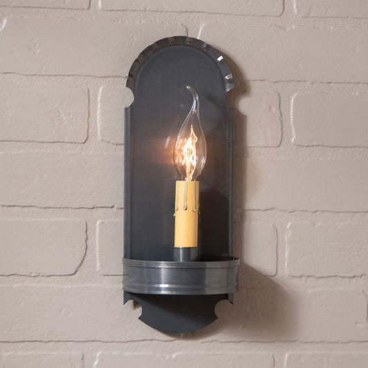 Tin wall sconce with one candelabra bulb on a brick wall