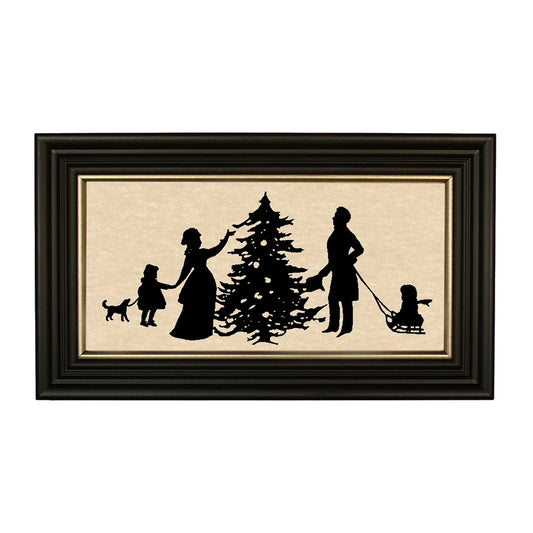 A black paper-cut silhouette of a family with a Christmas tree and decorations, framed in a solid ash wood frame with gold trim.