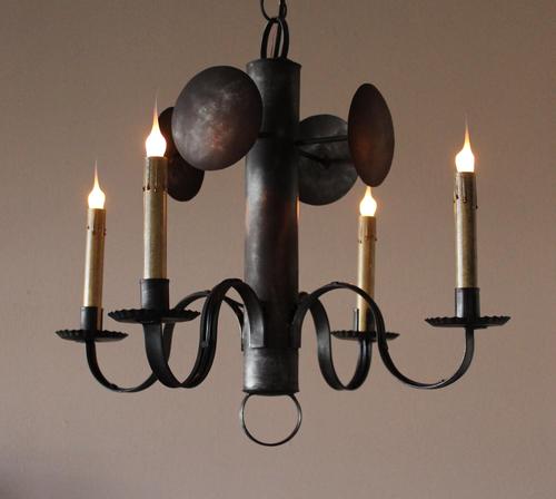 A Four Arm Tin Whaler Chandelier with a rustic design, featuring a central metallic structure with four hanging arms and candle-like bulbs.