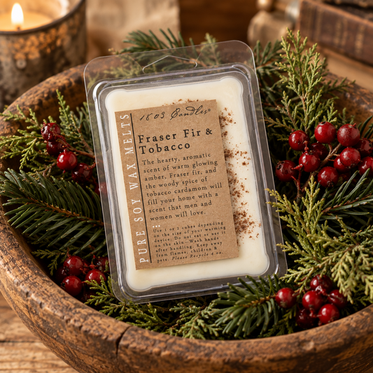 A packaged soy wax melt labeled 'Fraser Fir & Tobacco' by 1603 Candle Co., placed in a rustic wooden bowl surrounded by evergreen branches and red berries.