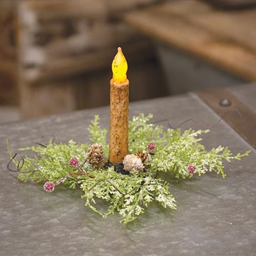 Frosty red berry and cone candle ring holding a battery operated taper on wood surface.