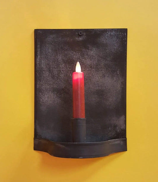 A black metal candle sconce mounted on a yellow wall, holding a red candle.