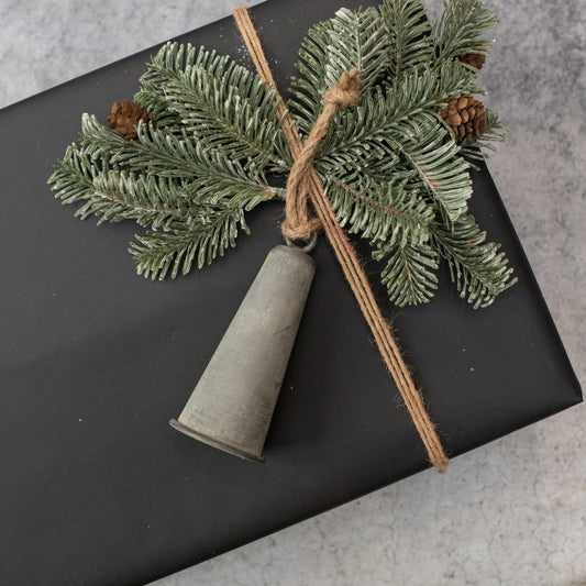 Galvanized large bell ornament on top of a black gift box with some greenery.