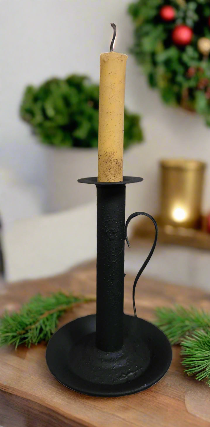 Black candle holder with a beige candle on a wooden surface, Christmas decorations in the background.