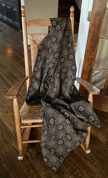 Dark patterned blanket draped over a wooden chair on a wooden floor.
