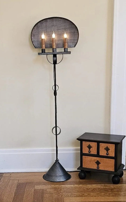 Black floor lamp with a round shade next to a small wooden cabinet against a beige wall.